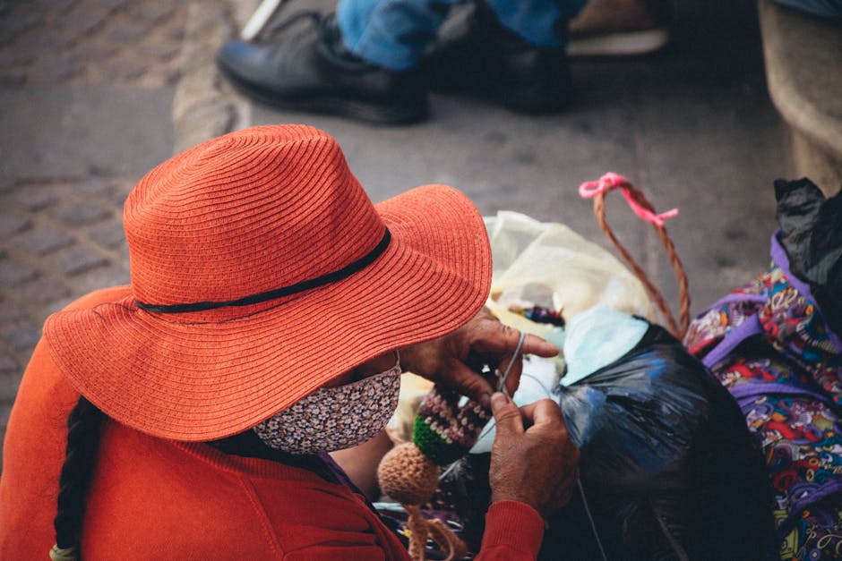 Candid shot of an elderly woman knitting on the streets of Guanajuato, Mexico, wearing a face mask and orange hat.