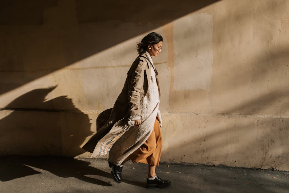 Side view of a stylish woman in a trench coat walking in sunny autumn weather.